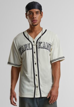 Kremna osnovna majica za baseball z črnimi detajli, z gumbi spredaj, kratkimi rokavi in napisom "KARL KANI" na prsih. Mehka, teksturirana tkanina.