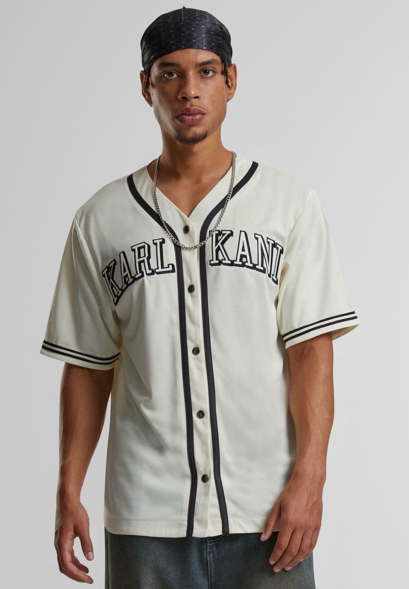 Tricou de baseball crem cu accente negre, buton în față, mâneci scurte și inscripția "KARL KANI" imprimată pe piept. Material moale, texturat.