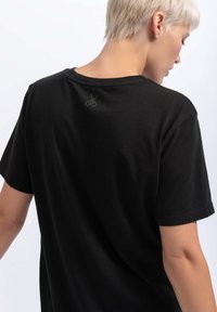 Zwarte katoenen T-shirt met een ronde halslijn en korte mouwen. Voorzien van een subtiele schaarontwerp dat op de rug is gedrukt, nabij de halslijn.