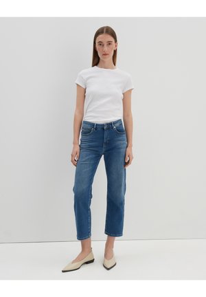 Weißes kurzärmliges Ripp-T-Shirt, blaue hochgeschnittene gerade Jeans und beiger spitz zulaufender Flats. Minimalistisches Design mit klassischer Passform.