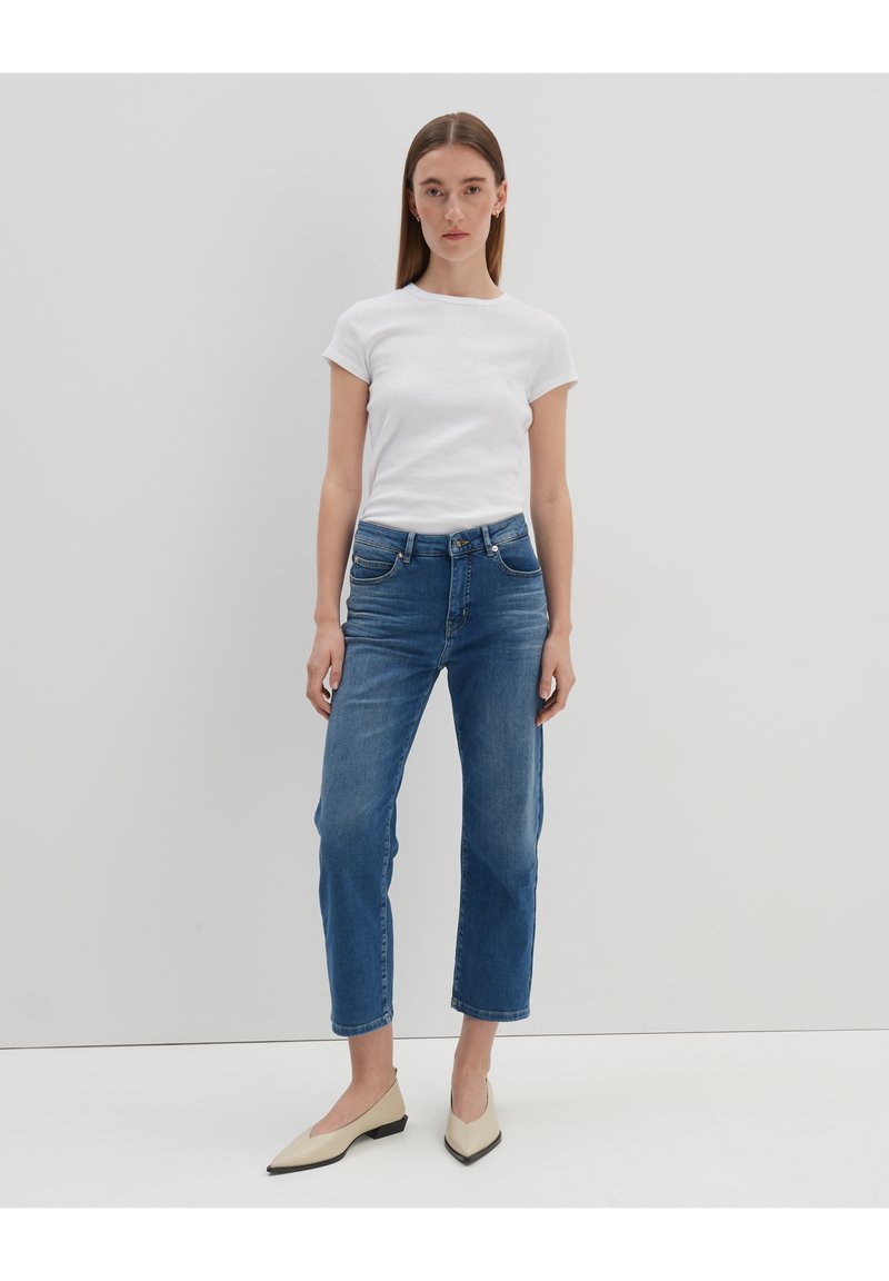 White short-sleeve ribbed t-shirt, blue high-waisted straight-leg jeans, and beige pointed-toe flats. Minimalist design with classic fit.