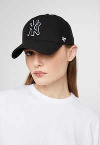 Svart baseballcaps i stoff, med en brodert hvit 'NY'-logo på fronten og et lite hvitt '47'-merke på siden.