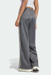 Sivé športové nohavice s voľným strihom, hladkou textúrou, bočnými pruhmi a elastickým pásom. Nohy mierne zúžené pri manžetách.