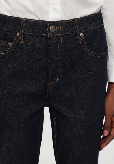 Mørke denimjeans med oransje sømmer, fem-lomme-design, metallhardware og en innsnevret passform. Livbåndet har en knappefeste.