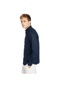 Camisa de manga larga azul marino con cuello abotonado, corte slim y textura sutil. Llevada con pantalones de color claro, se muestra el perfil lateral.