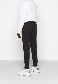 Schwarze Jogginghosen mit lockerem Sitz, mit einem bestickten Detail in der Nähe der Tasche und gerippten Bündchen. Kombiniert mit weißen Sneakers.