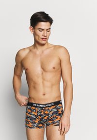 Herren-Boxershorts im Tarnmuster mit grünen, grauen und orangen Farbtönen. Aus dehnbarem Material mit einem schwarzen Bund, der mit "URBANCLASSICS" beschriftet ist.