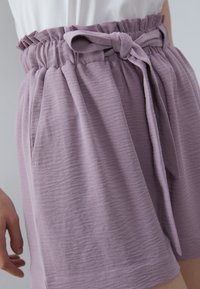 Shorts lilas clairs avec une finition texturée, dotés d'une taille haute, d'un bandeau élastique froncé et d'une ceinture en tissu. Comprend des poches latérales.