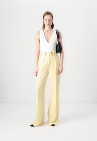 Valkoinen hihaton bodysuit, joka on yhdistetty korkeavyötäröisiin, leveisiin keltaisiin housuihin, joissa on etupainike, sekä mustaan käsilaukkuun, jossa on olkahihna.