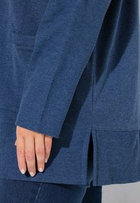 Marinblå tunika med texturerad ribbad ärm och sidospår. Materialet är mjukt med en lätt stretch, och har en framficka.