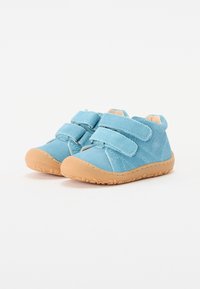 Blå ruskind babysko med tan gummisåler, der har to velcro-stropper og et afrundet design. Teksturerede detaljer og syninger er synlige.