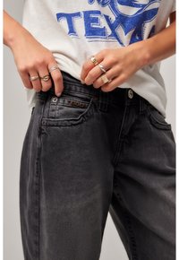 Black denim jeans featuring a subtle faded texture, five-pocket design, and a branded patch on the front pocket. Casual white graphic T-shirt.