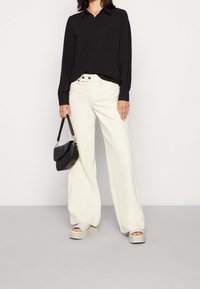 Black long-sleeve shirt with a collar, high-waisted cream wide-leg pants, chunky beige platform sandals, and a small black handbag.