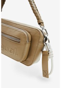 Beige Leder Umhängetasche mit zwei Reißverschlussfächern, einem strukturierten Tragegurt und Metallbeschlägen. Mit geprägtem Markenlogo an der Seite.