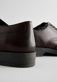 Des chaussures en cuir marron avec une finition lisse, ornées de détails brogue, à bout rond et avec un petit talon en caoutchouc noir.