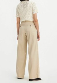 Breda beige byxor med hög midja och två bakfickor, parat med en krämfärgad stickad topp med ett texturerat mönster.