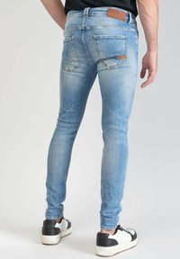 Vaaleansiniset farkut, joissa on kapeat lahkeet ja haalistumia, kaksi takataskua ja ruskea nahkaetiketti. Yhdistetty mustiin ja valkoisiin lenkkarit.