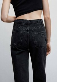 Jeans de mezclilla negros de tiro alto con un acabado desteñido, que cuentan con dos bolsillos traseros y un ligero desgaste. Detalles visibles en la cinturilla.