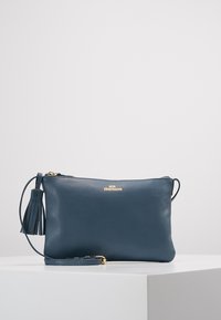 Una pochette in pelle blu navy con finitura testurizzata, hardware color oro, chiusura con zip e dettaglio in nappina. Include una tracolla staccabile.