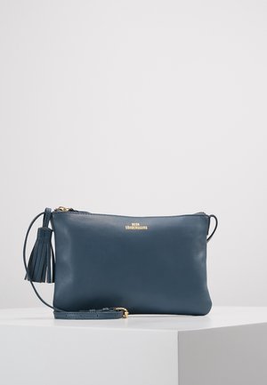 Pochette en cuir navy avec une finition texturée, quincaillerie dorée, fermeture éclair et accent à pompon. Comprend une bandoulière amovible.
