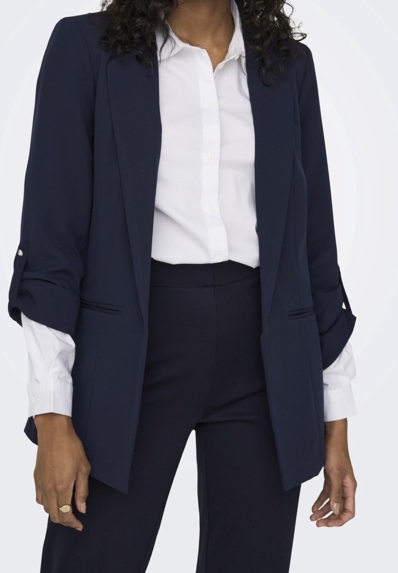 Blazer bleu marine en tissu léger avec une coupe ajustée, des revers crantés et des manches retroussées, accompagné d'une chemise blanche à boutons.