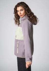 Hellviolette Fleecejacke mit einem mintgrünen Einsatz, einer Reißverschlusstasche auf der Brust und Kapuze. Strukturierter Stoff mit kontrastierenden Akzenten.