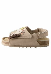 Braune Wildleder-Sandalette mit einem Ausschnittdesign, das ein verspieltes Tiermotiv und Fransenakzente auf dem Obermaterial aufweist. Die Korksohle sorgt für Halt.
