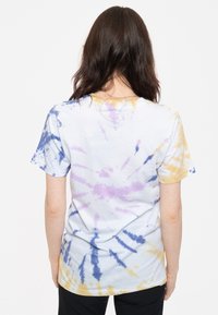 Tie-dye T-shirt in white, featuring purple, blue, and yellow patterns. Short sleeves and a relaxed fit, with a soft cotton texture.
