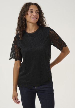 Black lace top featuring short, scalloped sleeves and a round neckline with floral patterns and textured fabric. Paired with dark jeans.
