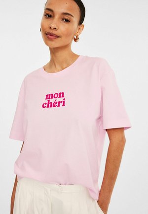 Lichtroze katoenen t-shirt met korte mouwen, voorzien van de tekst "mon chéri" in vet fuchsia lettertype aan de voorkant.