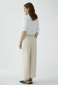 Beige wide-leg trousers with a textured design, paired with a white, rolled-sleeve blouse. Black shoes with a low heel complete the outfit.
