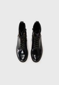 Bottines en cuir noir avec une finition brillante, dotées de détails en or, de lacets noirs et d'une fermeture éclair sur le côté.