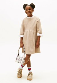 Robe-sweat beige avec une jupe évasée et un col blanc à volants. Des baskets marron, un sac à motifs et des chaussettes rayées complètent la tenue.