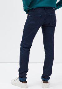Jeans blu scuro con vestibilità slim, dotati di tasche posteriori con un motivo sottile, abbinati a sneakers bianche e un dettaglio di risvolto.