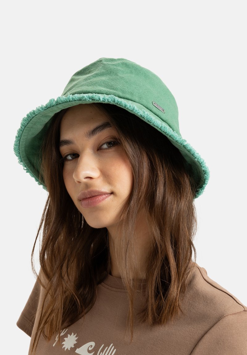 Zelený klobouk typu bucket vyrobený z měkké tkaniny, s třepící se hranou a malým kovovým logem na boku.