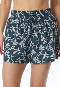 Teal shorts met een wit botanisch patroon, voorzien van een elastische tailleband en een trekkoord. De stof lijkt lichtgewicht en soepel te zijn.