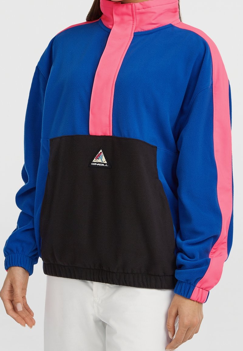 Personne portant un pull bleu et noir avec des accents roses et un patch logo O'Neill sur la poche avant.