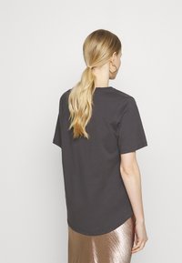 Camiseta de algodón de color gris oscuro con mangas cortas, escote redondo y dobladillo ligeramente curvado, combinada con una falda brillante de bronce.