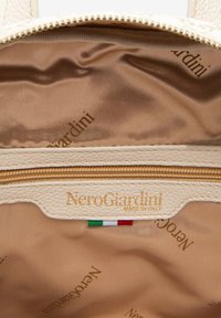 Interno in pelle beige di una borsa con cerniera dorata. Presenta il nome del marchio "NeroGiardini" in oro e un piccolo dettaglio con la bandiera italiana.