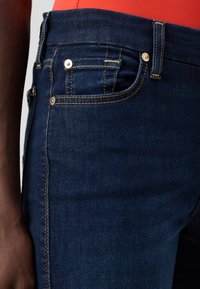 Σκούρο μπλε τζην παντελόνι με χρυσά ραφά, λεπτομέρειες στις μπροστινές τσέπες και στενή εφαρμογή. Διαθέτει κλασική ζώνη μέσης και διακοσμητικές βίδες.