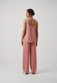Rosa, ermeløs topp med firkantet rygg, paret med løstsittende, matchende bukser. Stoffet ser glatt og lett ut.