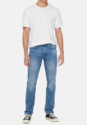 Lichtblauwe denim jeans met een rechte pasvorm, subtiele vervaging en een klassiek vijf-pocket ontwerp, gecombineerd met een plain wit t-shirt en zwarte sneakers.