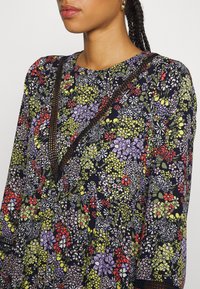 Vestido com padrão floral em fundo azul-marinho, apresentando flores vermelhas, verdes e roxas. Decote detalhado com costura preta e mangas longas.