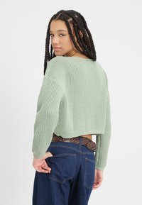 Menta zöld, kötött pulóver laza szabással, cropped fazonnal és széles ujjakkal, sötét farmernadrággal és fonott barna övvel párosítva.
