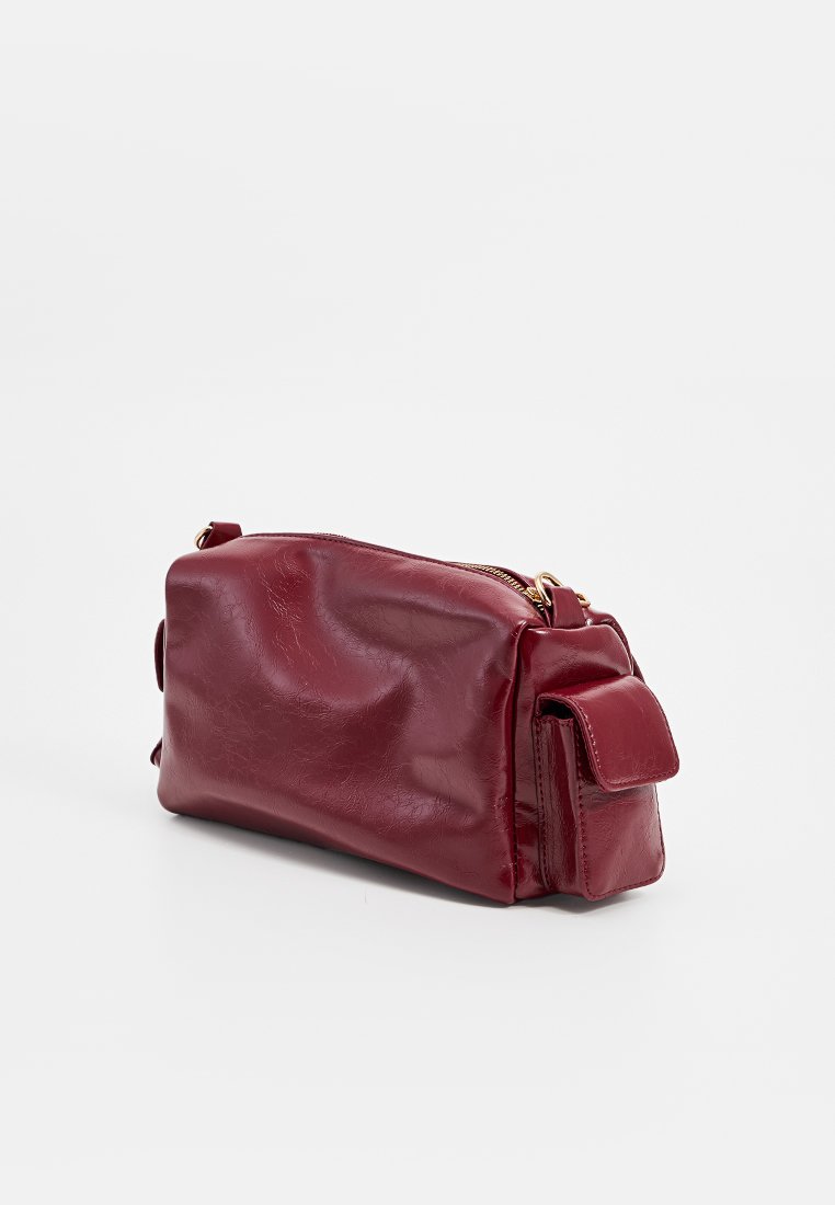 Rote synthetische Lederhandtasche in rechteckiger Form, mit Reißverschluss und einer Seitentasche. Bietet eine glatte Textur und minimales Zubehör.