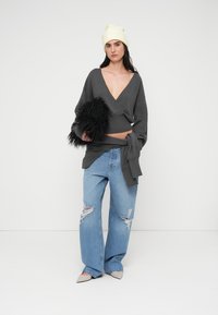 Γκρι πουλόβερ τύπου wrap, φθαρμένο ανοιχτό μπλε τζιν με φαρδιά μπατζάκια, μπεζ ψηλοτάκουνα με μυτερή μύτη και λευκό πλεκτό σκουφάκι, με μια μαύρη τσάντα από χνούδι.