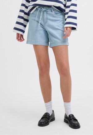 Persoană care poartă pantaloni scurți din denim albastru deschis, cu o curea legată, șosete albe, mocasini negri și o cămașă cu mânecă lungă, albă cu dungi bleumarin.