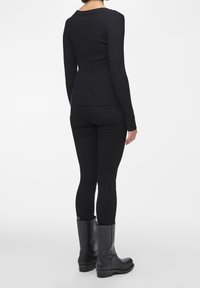 Black ribbed long-sleeve top paired with black fitted jeans and tall black leather boots, viewed from the back. Textured fabric and simple design.