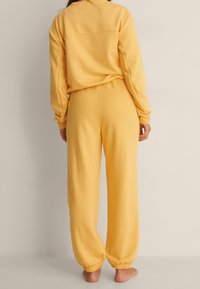 Felpa gialla e pantaloni abbinati realizzati in materiale morbido, con una vestibilità rilassata, polsini elasticizzati e vita a coste.