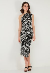 Black and white patterned dress with one shoulder, fitted design, knee-length, made from a smooth fabric. Worn with black sandals.
